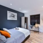 Dark grey and orange themed bedroom with glass desk and laminated floor